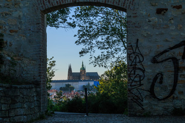 Prague Castle from the viewpoint Petrin in district Mala Strana on sunny day with blue sky with a view through a stone gate and trees and shrubs