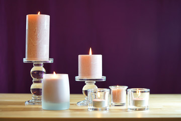 Aromatherapy composition with pink candles on table against purple background, shallow focus.