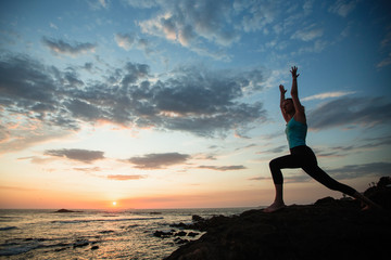 Fototapeta premium Young fitness woman sees off the sun on the ocean coast. Exercises, yoga and training. .