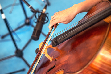 Closeup of cello strings and a hand playing with a bow during studio recording. © eshana_blue