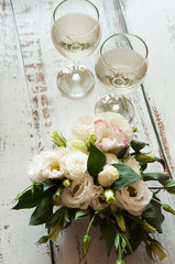 Glasses with wine on a white rustic wooden background with a bouquet of flowers. Wedding table greeting card. Wedding invitation light background.