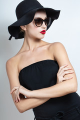 beautiful model in a black hat and sunglasses. Black dress. arms crossed over his chest.