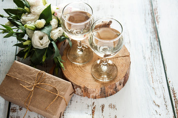 Glasses with wine on a white rustic wooden background with a bouquet of flowers and craft gift. Wedding table greeting card. Wedding invitation light background.
