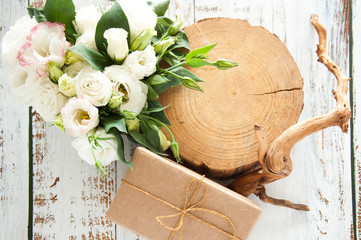 White rustic wooden background with a bouquet of flowers and craft gift. Wedding table greeting card. Wedding invitation light background.