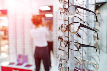 Eyeglasses shop. Stand with glasses in the store of optics. Woman trying on glasses in optical store