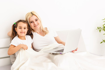 Smiling mother and daughter using laptop in bed at home