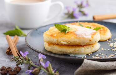 Cheese pancakes on a blue ceramic plate and a cup of coffee on a gray concrete background.