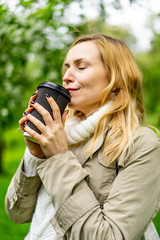 Beautiful blond woman drinking aromatic coffee of the blur green park background