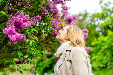 Beautiful blond woman posing outdoors at the blur spring park of violet and white lilac background