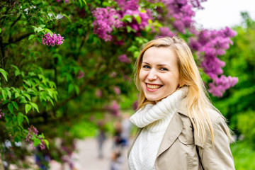 Fototapeta premium Beautiful blond woman posing outdoors at the blur spring park of violet and white lilac background