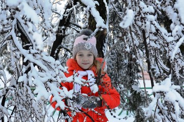 little girl looks at the photographer and poses among the snowy tree branches