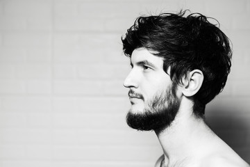 Black and white portrait of young bearded guy with disheveled hair on white background.