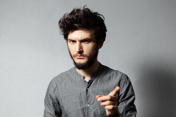 Fototapeta premium Portrait of young bearded serious guy with disheveled hair, having a new idea, pointing finger away.