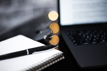 Close-up of pen and notebook on black desk of glass near laptop and sunglasses.