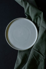 white handmade plate with green fabric napkin on dark background, handmade pottery plate on black table, empty plate, mockup, copyspace, empty space