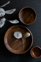 wooden dishes with green cloth napkin and eucalyptus leaves on dark counter, collection of teak dishes at craft fair, beautiful wood bowls and plate on black background, copyspace, copy space