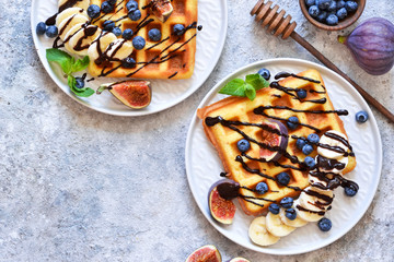 Vanilla waffles with chocolate sauce with peaches and berries on a kitchen stand. View from above.