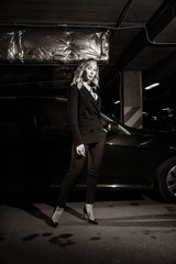 Noir film style woman in a black suit posing in an undergound car park....