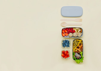 Open lunch box with vegetable pasta and chicken meat, berries, nuts and candies on light yellow background
