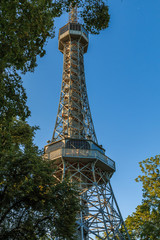 Old Petrin radio tower made of steel in Prague on the Petrin hill in the district of Lesser Town with viewing platform in summer with blue sky and trees in the foreground