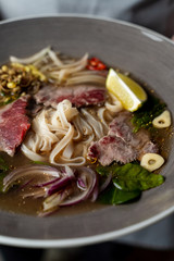 Holding a bowl with raw beef tenderloin soup with rice noodles, onion, garlic, chilli pepper, seedlings and mint