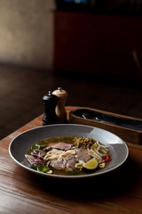 Side view of raw beef tenderloin soup with rice noodles, onion, garlic, chilli pepper, seedlings and mint in daylight