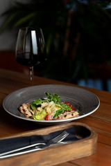 Side view of classic caesar salad with grilled chicken fillet, greens and cherry tomatoes with a glass of red wine