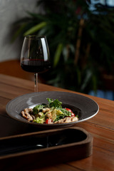 Side view of classic caesar salad with grilled chicken fillet, greens and cherry tomatoes with a glass of red wine
