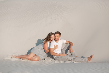 Romantic pair sit on white sand and huggins, in desert.