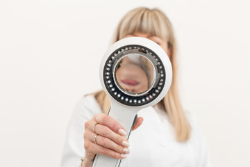 Portrait of a doctor trichologist dermatologist looking at a dermatoscope. Focus on the hand with a...