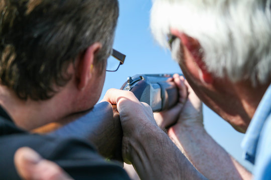 A man is given guidance in clay pigeon shooting from another man, holding a rifle in preparation of firing at a clay