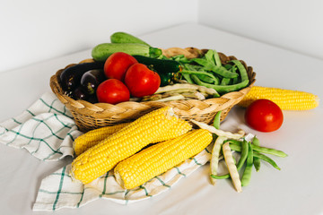 a group of fresh vegetables in a basket, there are tomatoes, zucchini, eggplant, yellow and red bean, cucumber and corn
