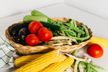 a group of fresh vegetables in a basket, there are tomatoes, zucchini, eggplant, yellow and red bean, cucumber and corn