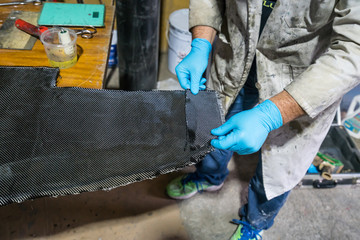 Man with protections on hands, eyes and mask, repairing a piece of carbon and epoxy resin.
