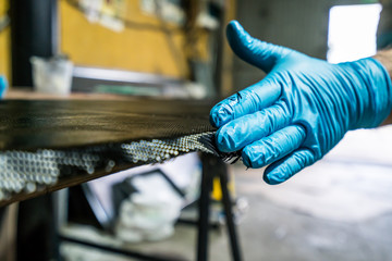 Man with protections on hands, eyes and mask, repairing a piece of carbon and epoxy resin.
