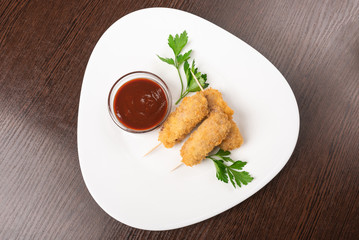 Korndog on skewers, breaded and with sauce. On the plate.