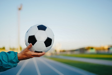 Man's hand holding soccer ball on running track