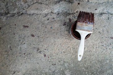 White brush with brown paint on the bucket on the ground on concrete background high angle