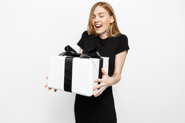 Fototapeta premium Happy young girl in black dress holding Black Friday gifts. A woman on a white background holds a gift box with a black ribbon