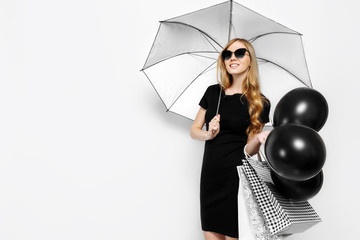 Elegant young beautiful girl in black dress posing with umbrella and shopping bags and black balloons on white background. black Friday