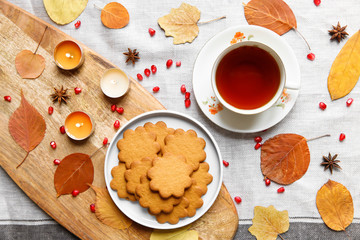 Top view of a cozy homemade tea party.  Autumn composition. Cup of hot tea, Gingerbread cookie, burning candles, yellow fallen leaves, seeds pomegranate, anise on a linen tablecloth. Flat lay