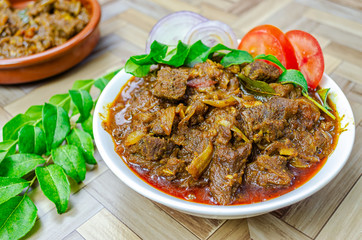 Traditional Kerala Beef Curry garnished with curry leaves, sliced onions and tomatoes