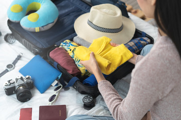 Preparing suitcase for summer vacation trip. Young woman checking accessories and stuff in luggage on the bed at home before travel.