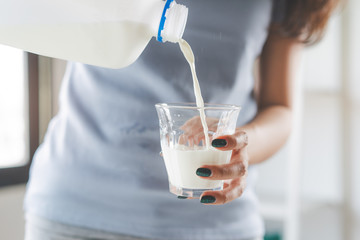 Young woman pouring milk to the glass in in the kitchen in the morning.