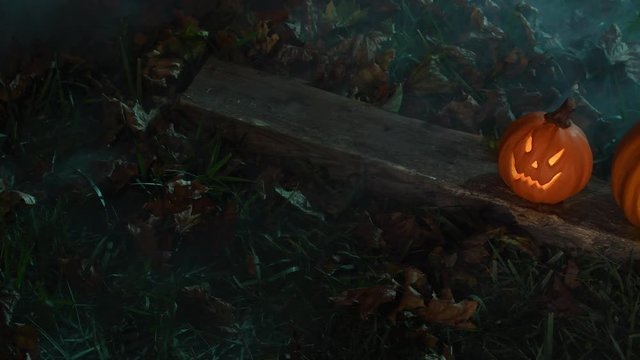 An overhead slider pair of glowing scary Jack O&rsquo;Lantern sitting in the grass with a red eyed raven in the background as a fog rolls through at night