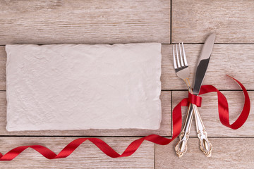 Close up on table settings with a decorative red bow on silverware, directly above.