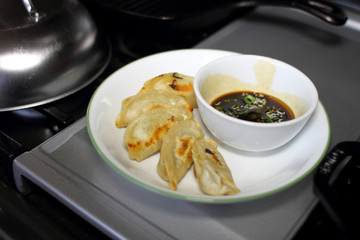 Pan fried dumplings with soy dipping sauce on a plate, resting on the stove top in a home kitchen.