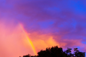 Obraz na płótnie Canvas Rainbow cutting through sunsetting storm cloud rolling overhead.