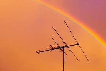 Residential tv antenna pointing directly through rainbow overhead - Powered by Adobe