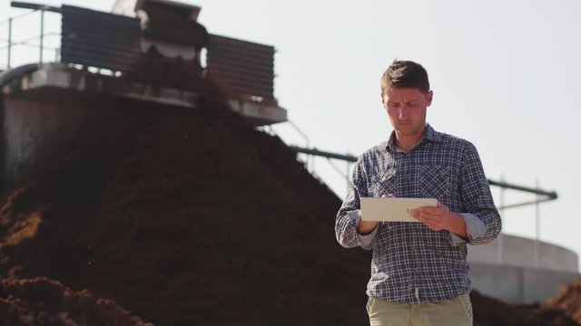 Slow motion of an young agronomist is using advanced technology with a tablet for controlling a quality of an organic cow manure compost used for agricultural soil cultivation and for biogas.